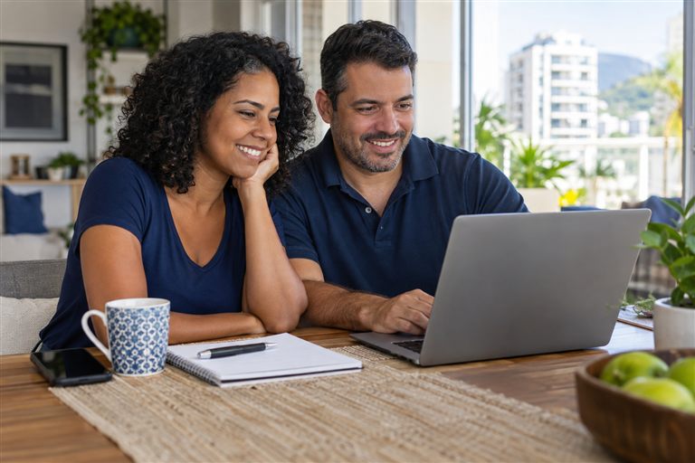 Casal organizando as finanças pessoais com um notebook em casa.
